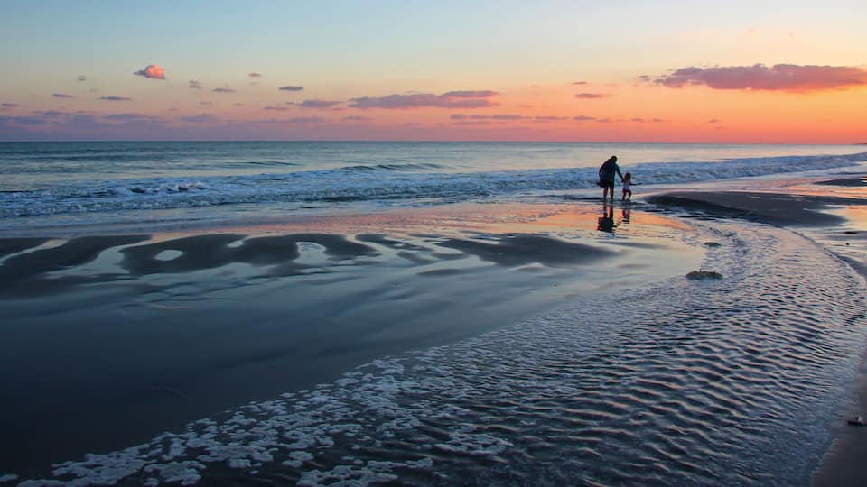 A beach at sunset with waves, a person, and a child.