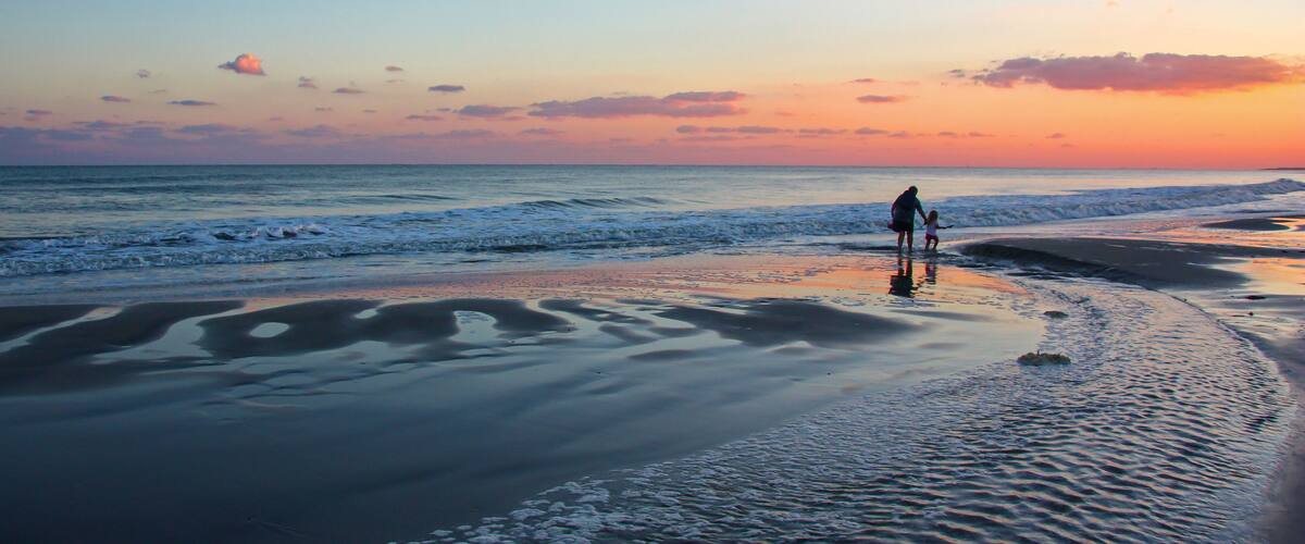 A beach at sunset with waves, a person, and a child.