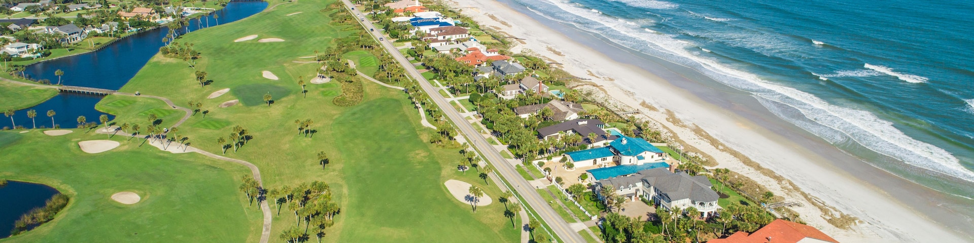 Un paisaje costero con un campo de golf, una playa y edificios residenciales.