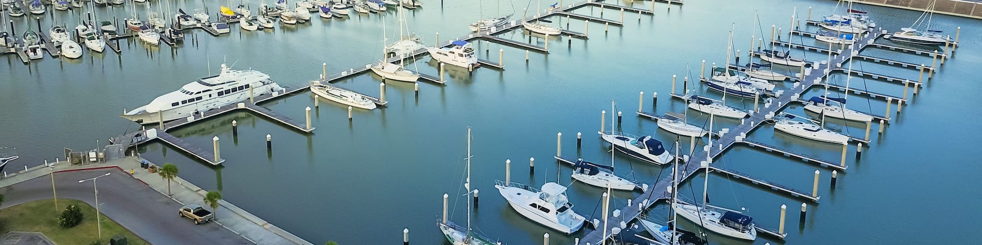 Panorama aerial view waterfront harbor Corpus Christi with marina and downtown skylines in background. Yacht, sailboat is moored at the quay. Top pier speedboat in marina lot filled full row of boat