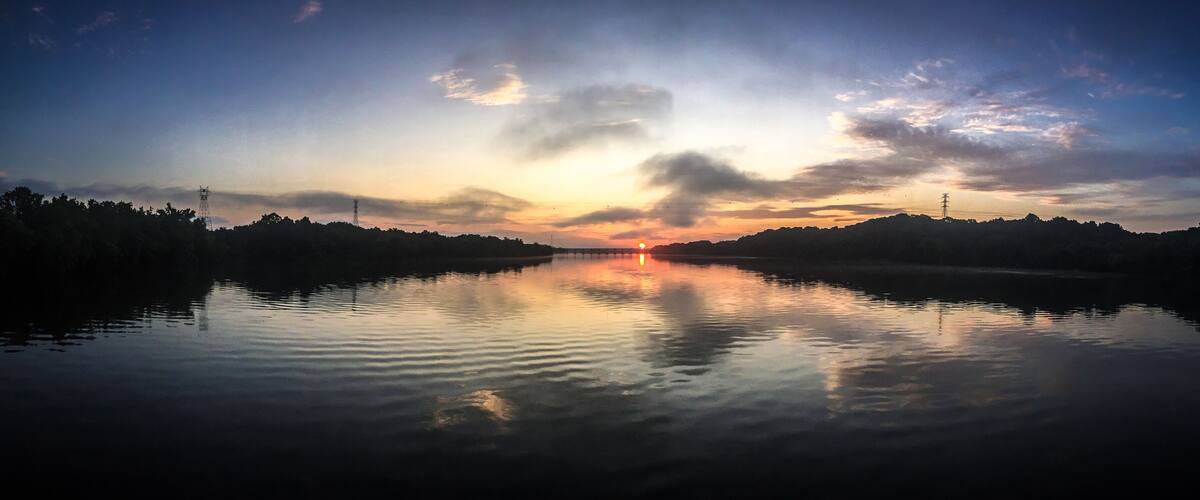 A calm river at sunset with a clear sky and distant power lines.
