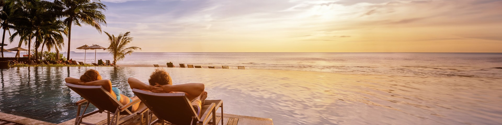 beach vacations, young couple in luxury hotel resort, man and woman relaxing near swimming pool at sunset