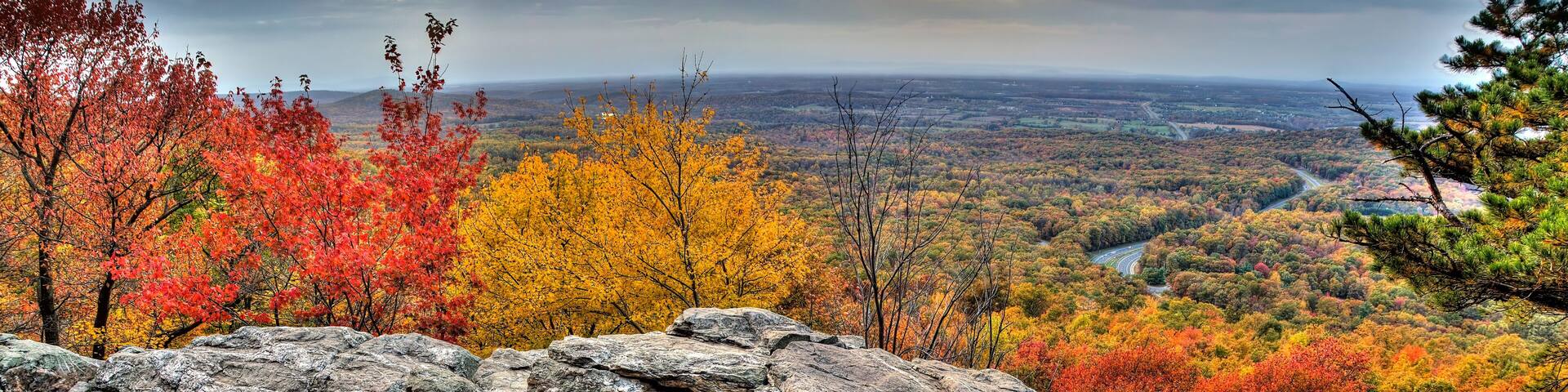 A mountainous landscape with autumn foliage, rocky outcrops, and a valley below.
