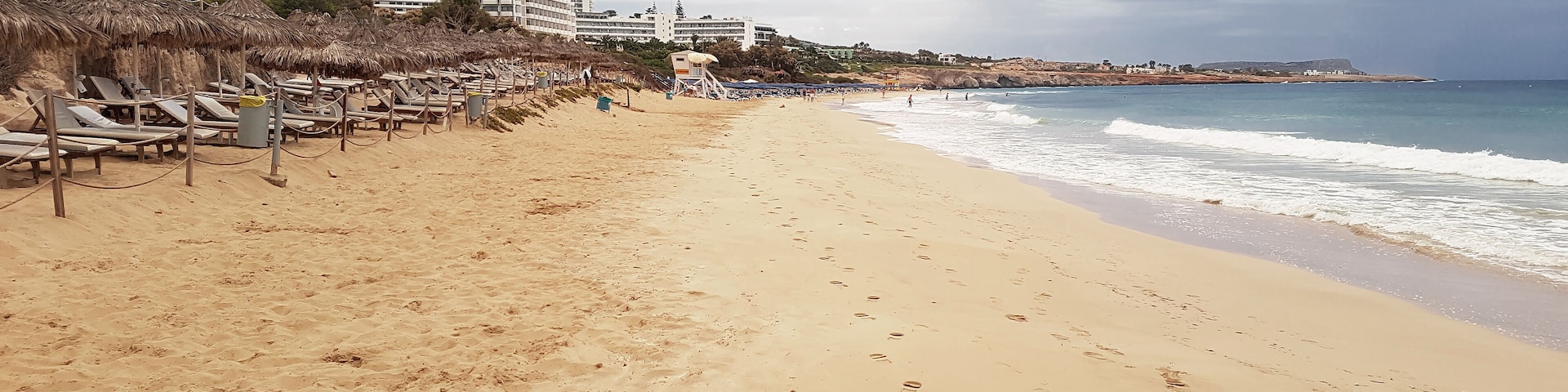 View of the sandy beach and hotels of the sea coast in Cyprus against the backdrop of a gloomy sky..