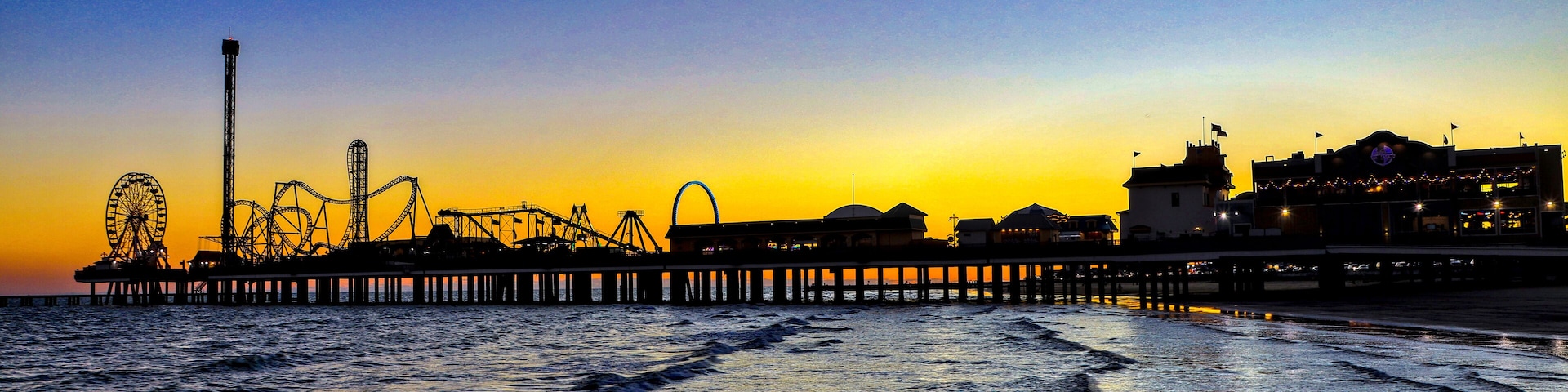 Galveston, Texas - 11-23-2024. A panorama of an amusement park on a large pier stretching out into the Gulf of Mexico at sunset.