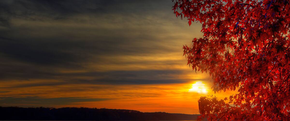 A sunset over a calm lake with red autumn leaves on the right.