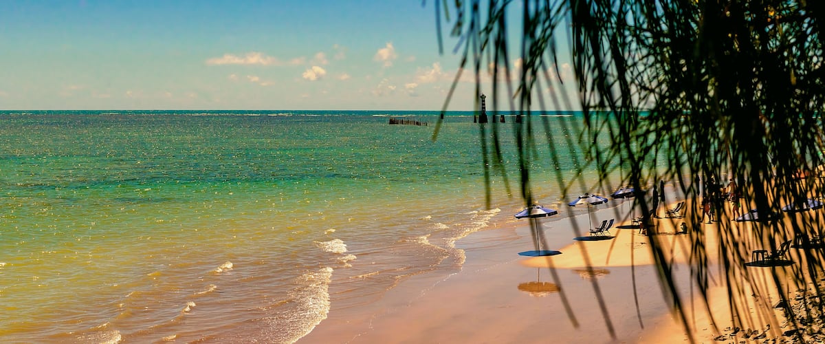 A beach with clear turquoise water, a sandy shore, and a few umbrellas and chairs.