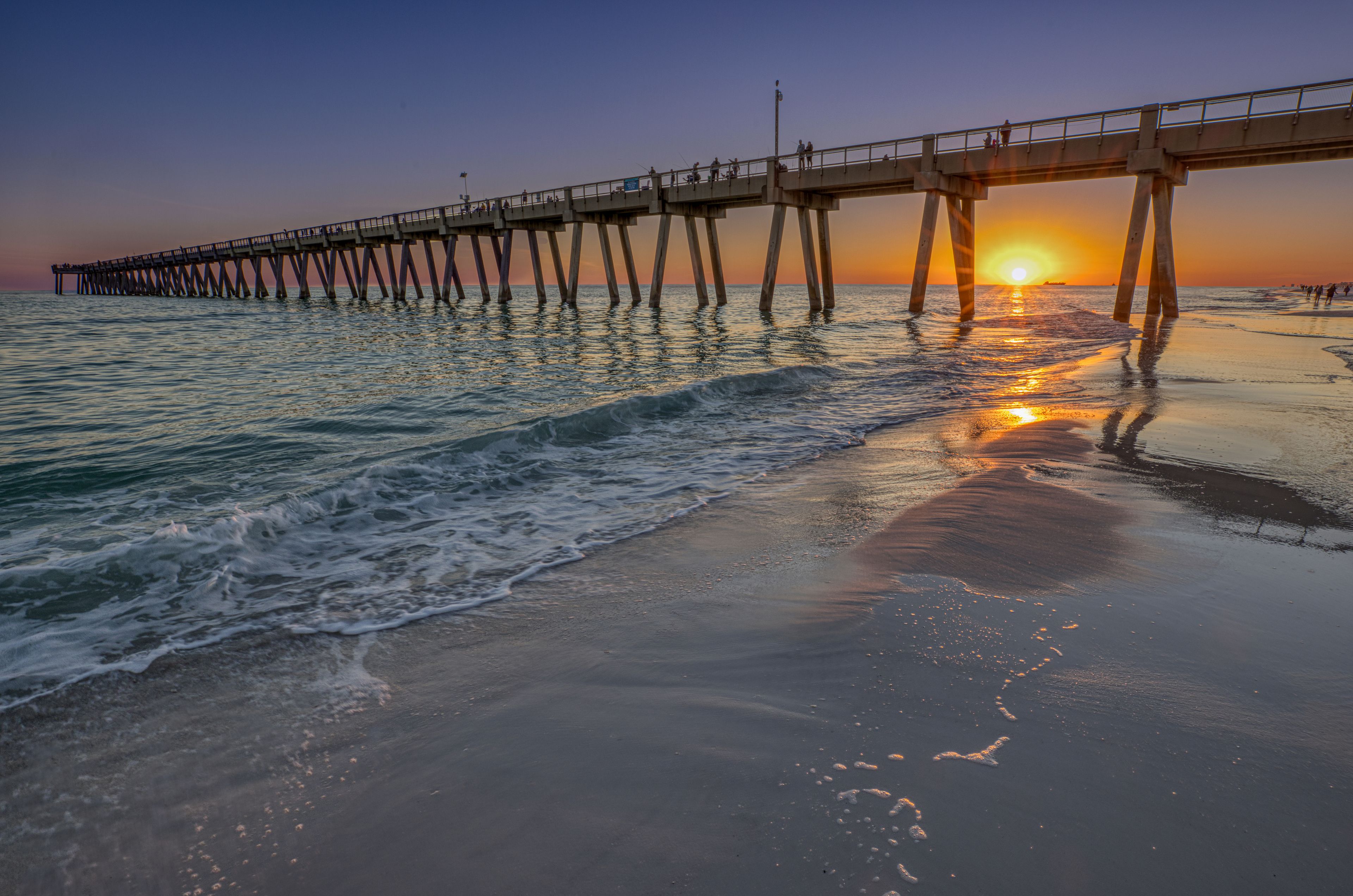 Un muelle se adentra en el océano con el sol poniéndose al fondo.