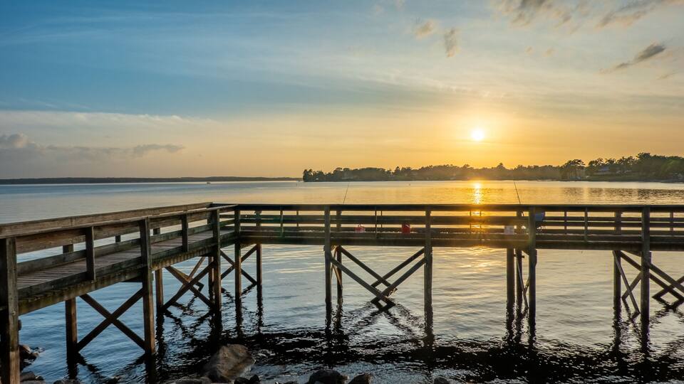 A wooden pier extending into calm water during sunset.