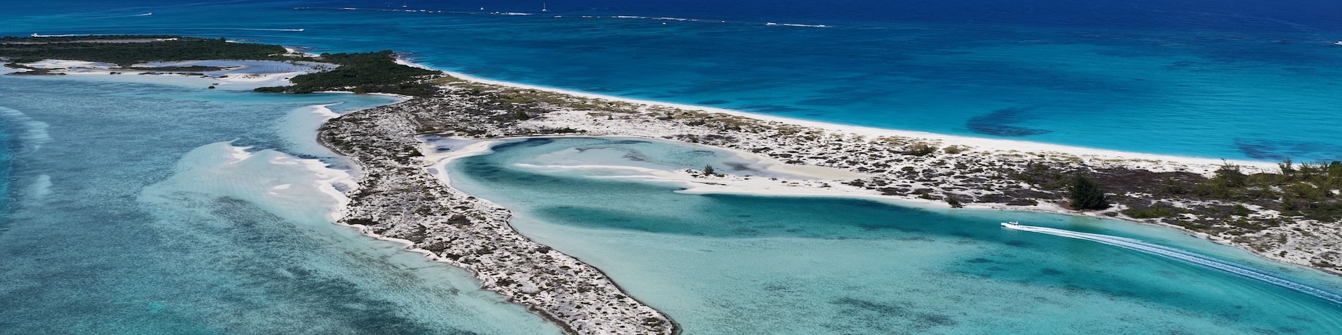 A turquoise lagoon with a white sandy beach and a small island with a rocky shoreline.