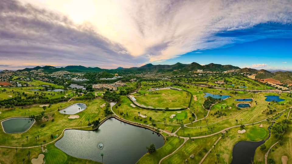 Un campo de golf con varios estanques y montañas al fondo.