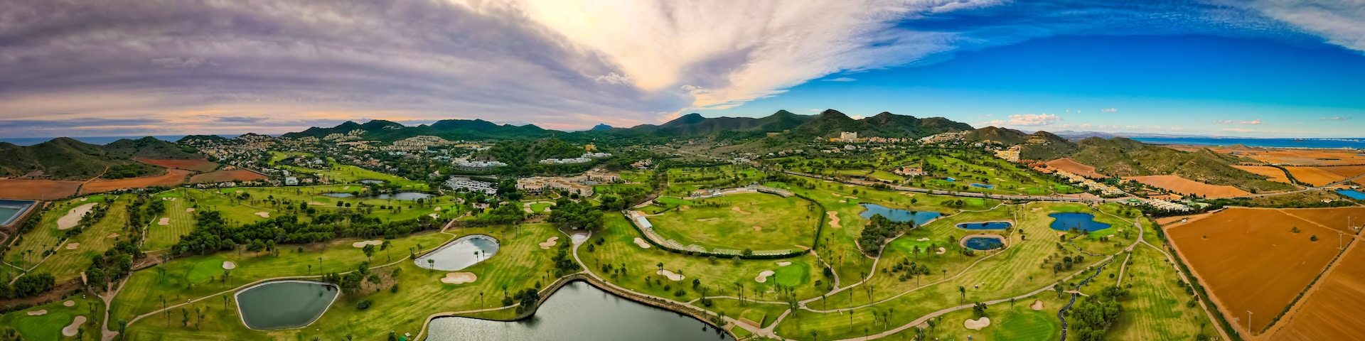 A golf course with multiple ponds and a mountainous backdrop.
