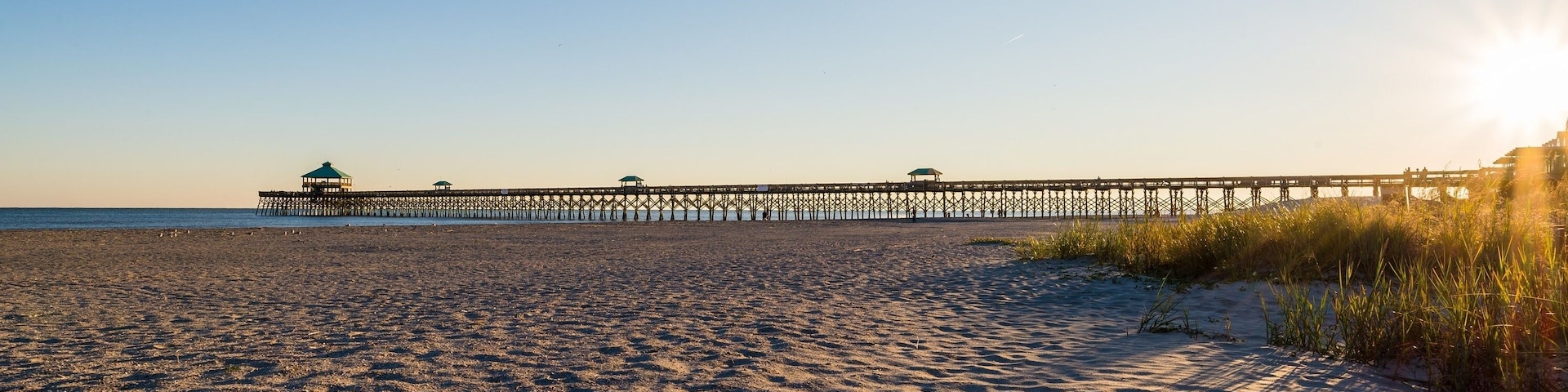 Ein Strand mit einem Steg, der ins Wasser führt, mit mehreren überdachten Bereichen.