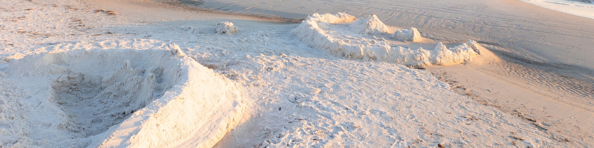 Two sandcastles on a white beach on a coast with a soft, white light and clear sky.