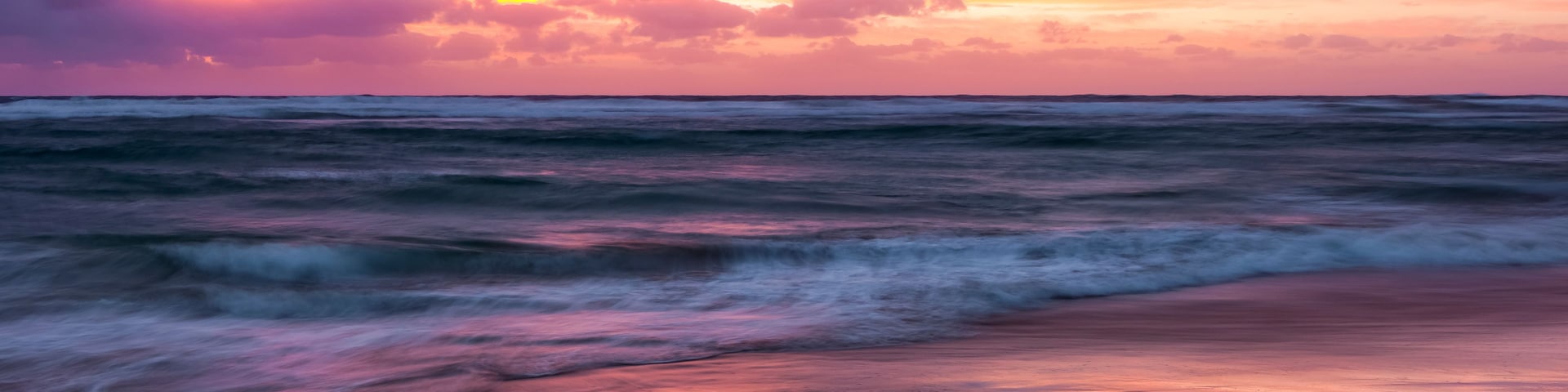 Ein Strand mit Felsen und Wellen bei Sonnenuntergang.