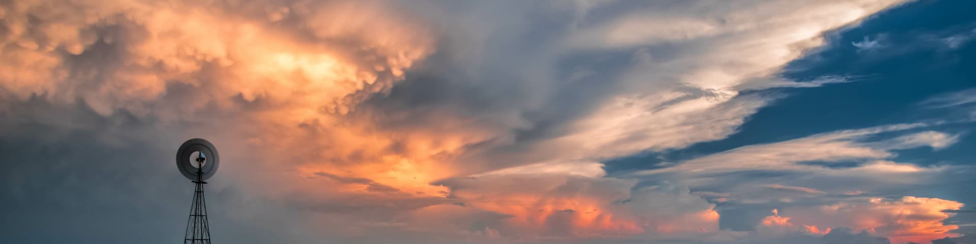 A windmill in a field with a dramatic sunset sky.