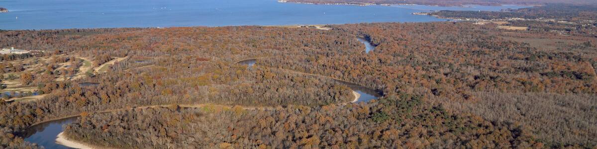 A river winding through a forested area with a large body of water in the background.