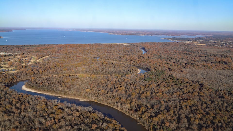 A river winding through a forested area with a large body of water in the background.