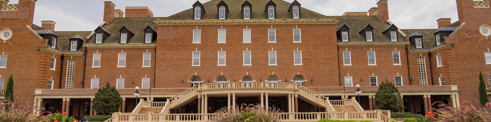 A large brick building with a central tower, a formal entrance with stairs, and well-maintained gardens.