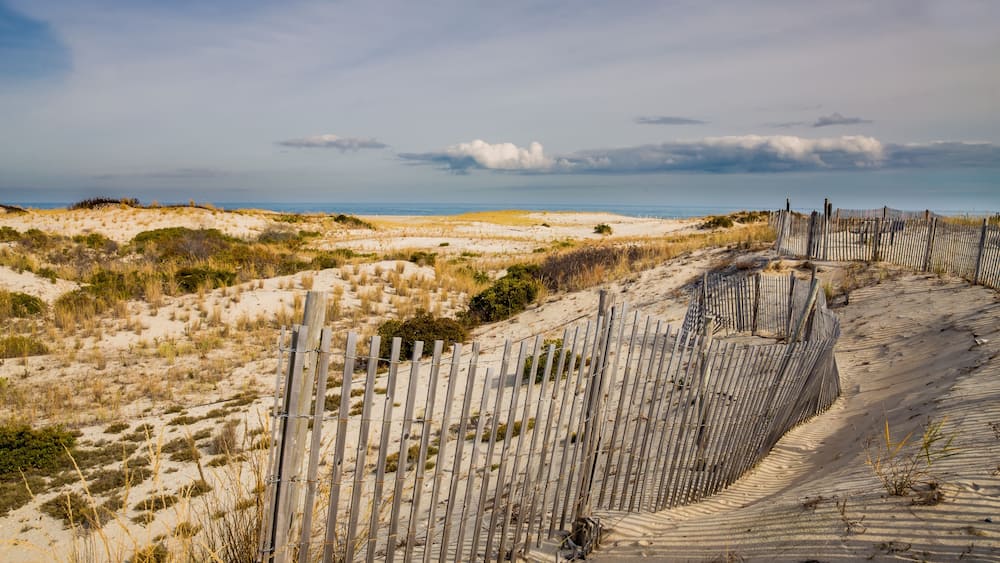 A sandy beach with a wooden fence and dunes.