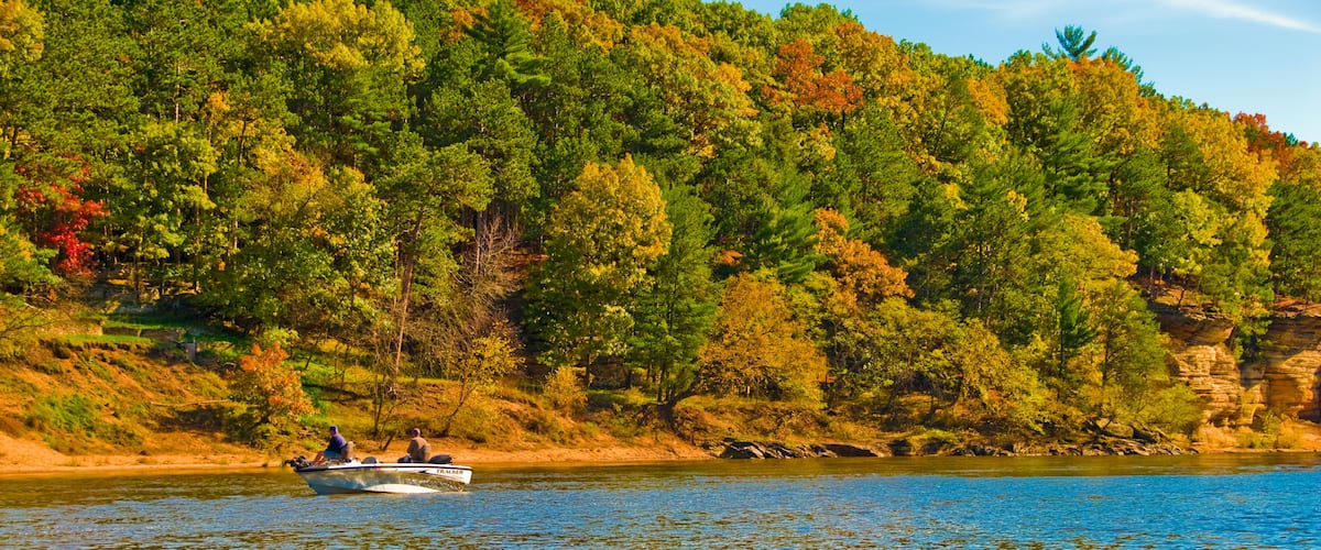 A boat on a calm river with a forested hillside in the background.