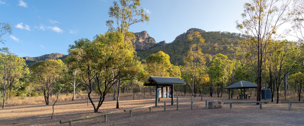 A park with picnic tables, a shelter, and a rocky mountain in the background.