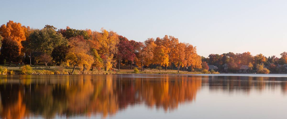 A calm lake with autumn trees reflecting in the water.