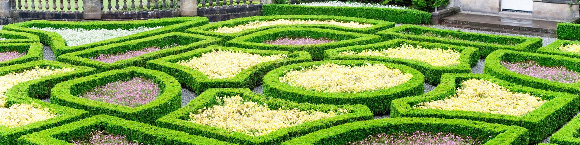 A formal garden with geometric hedges and a historic stone building.
