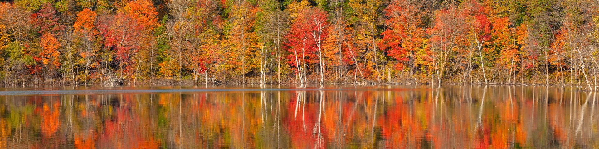 A lake reflecting autumn trees with red, orange, and green foliage.