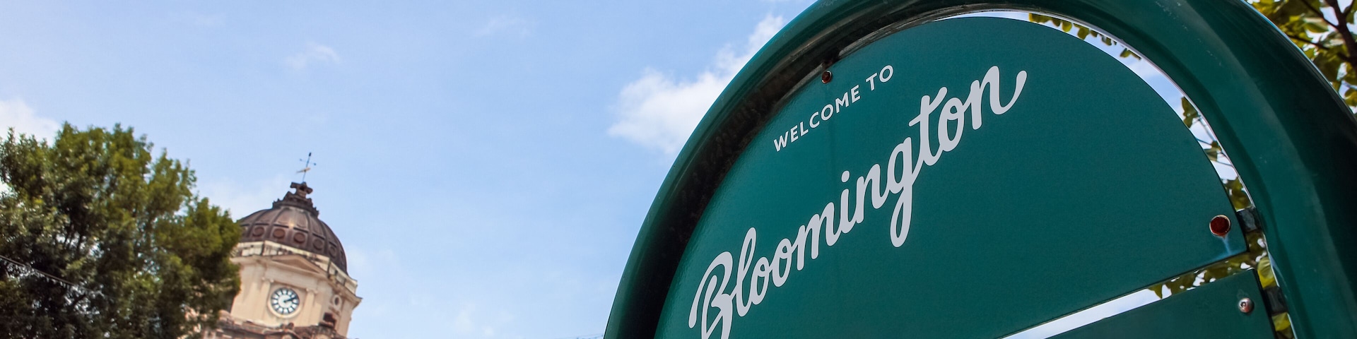 Welcome to Bloomington Indiana sign with downtown courthouse in the background