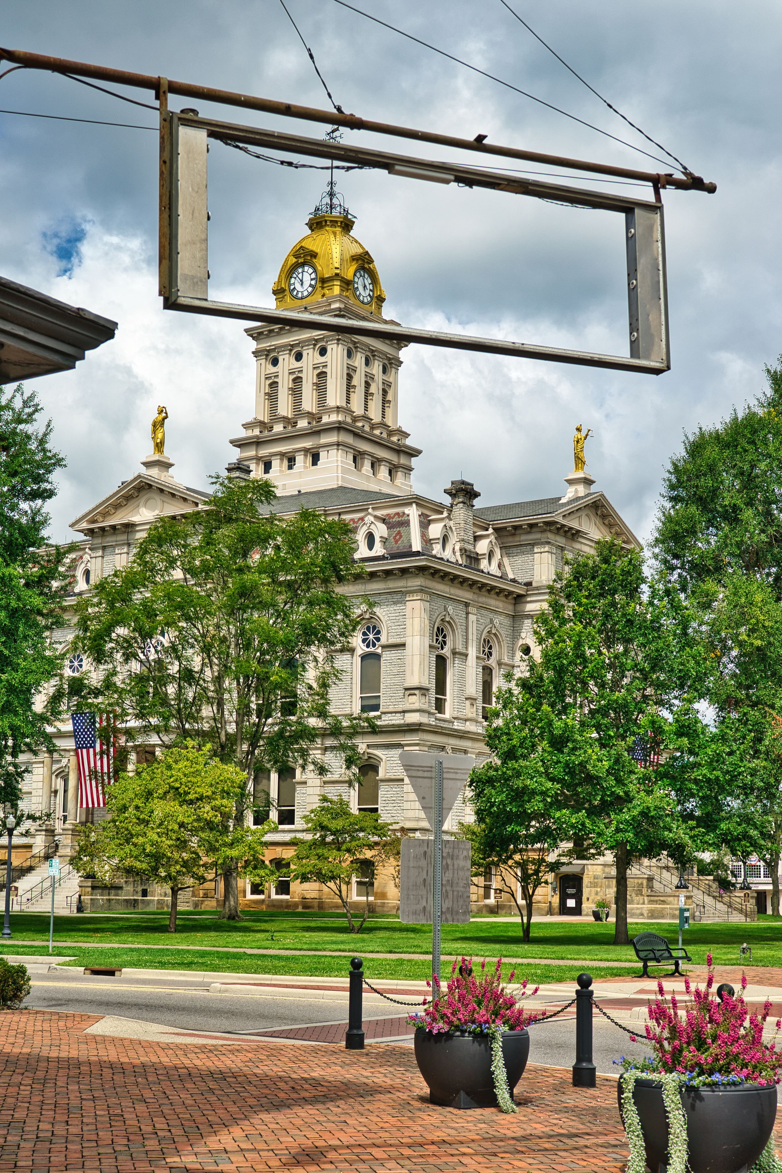 A historic building with a prominent dome and statues, surrounded by trees and a brick pathway.