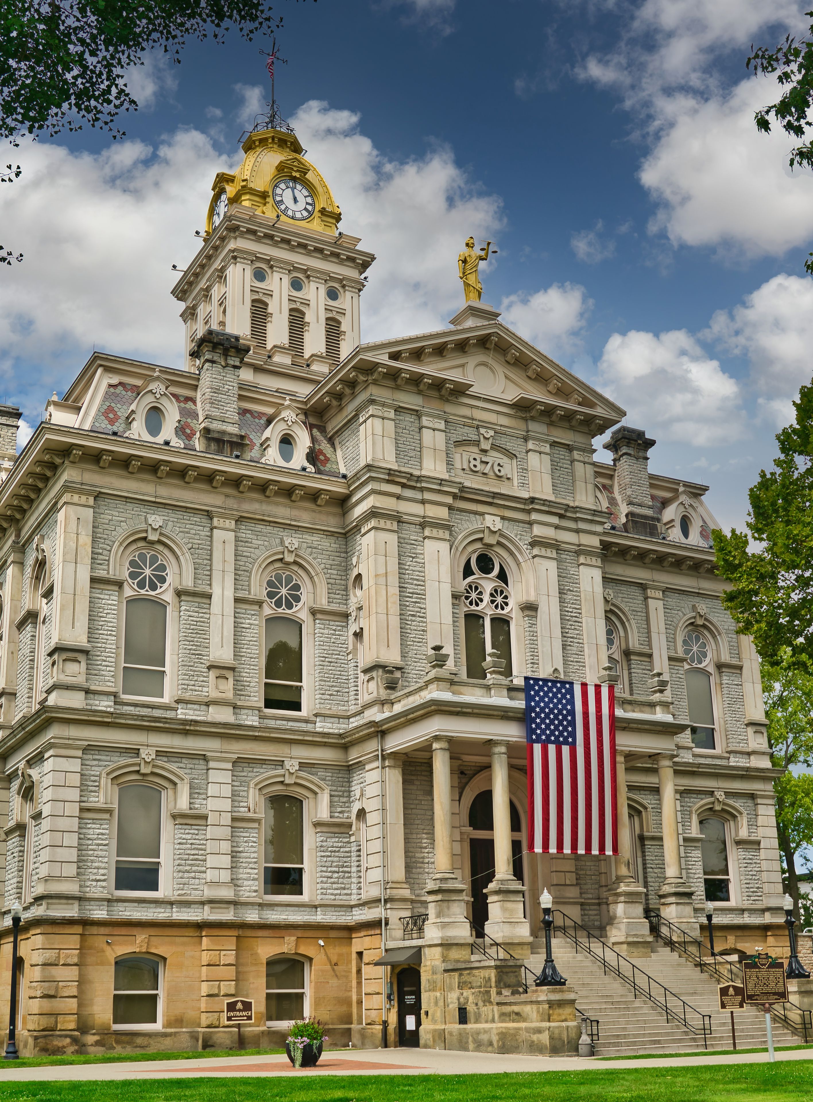 A historic building with a clock tower, a statue, and an American flag.