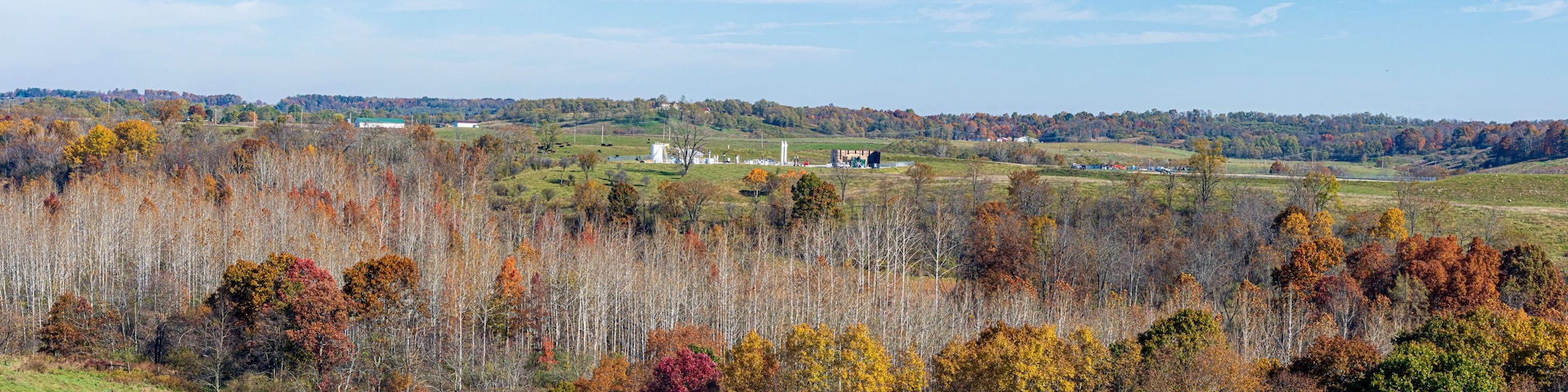A rural landscape with autumn foliage, a wind turbine, and a distant hill with a water tower.