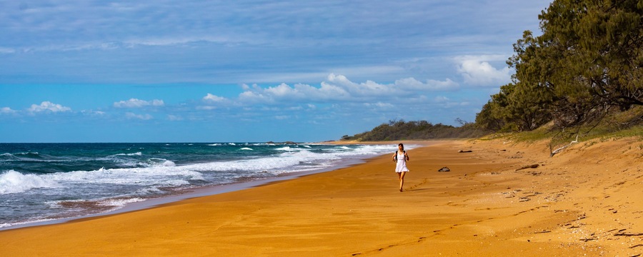 A beach with a woman walking along the shore.