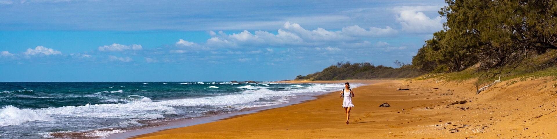 beautiful long haired girl in white dress walking lonely on the empty beach; walking on pristine beach with orange sand in deepwater national park near agnes water, australia