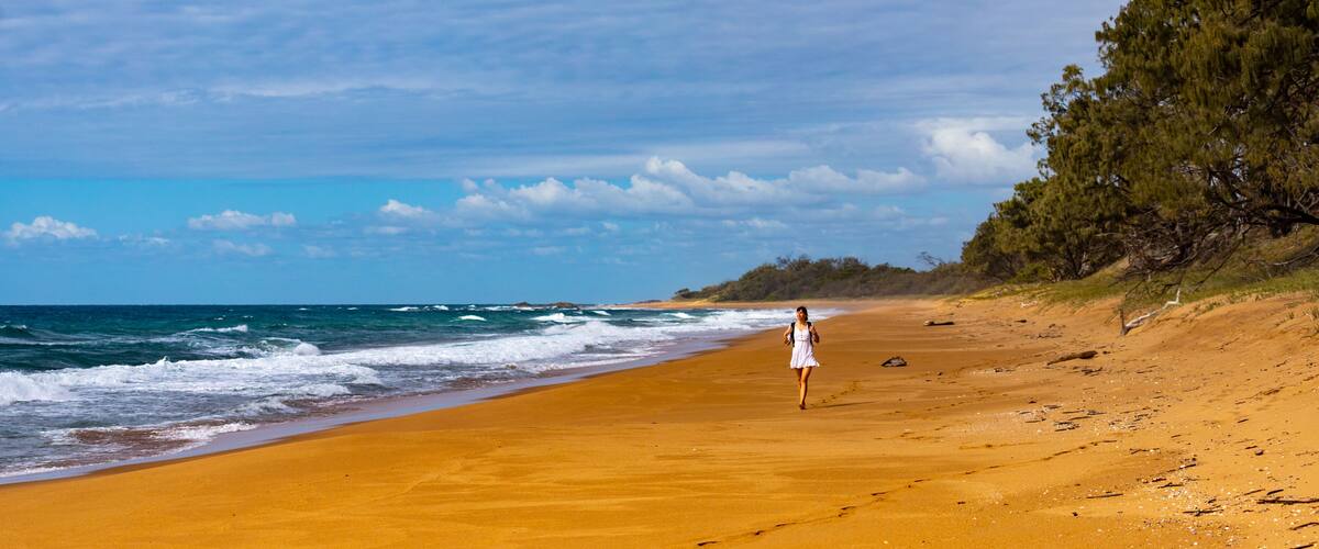 A beach with a woman walking along the shore.