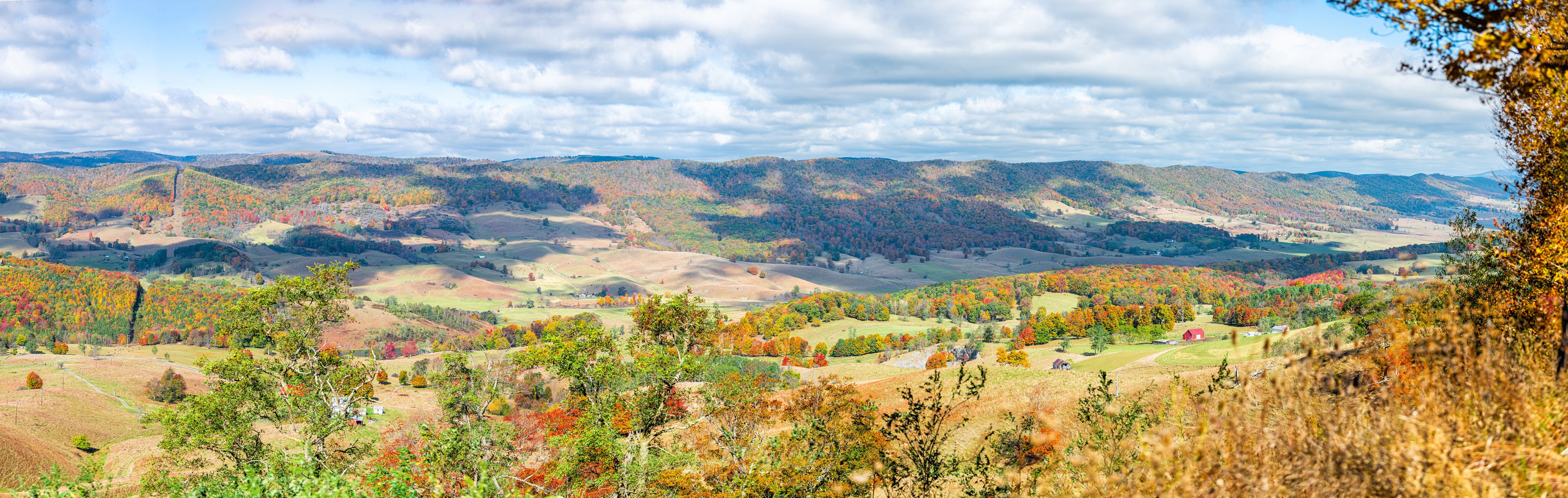 A valley with rolling hills, autumn foliage, and scattered buildings.