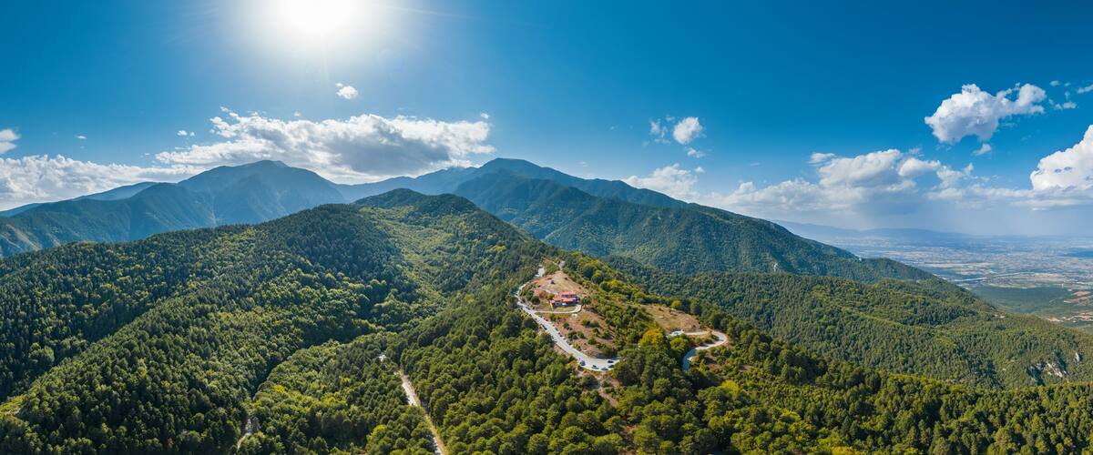 Aerial panorama of Greece mountains, green forest, blue sky, sun