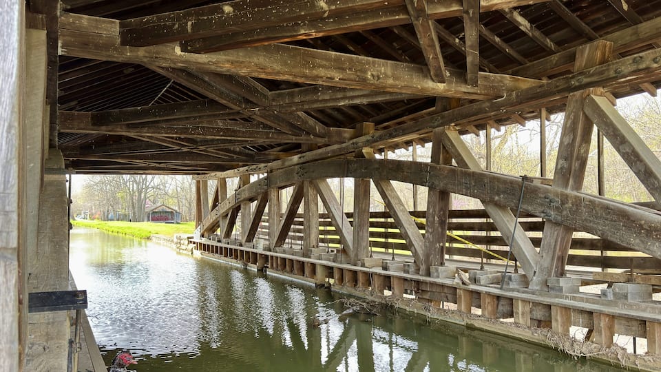 A wooden bridge over a calm river with ducks swimming below.