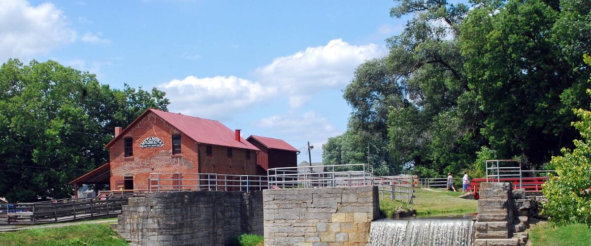 A brick building with a red roof, a stone bridge, and a waterfall.