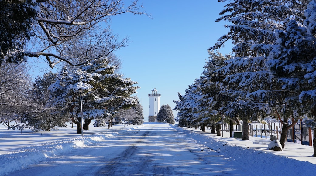 A snow-covered road with a lighthouse in the distance, surrounded by snow-laden trees.