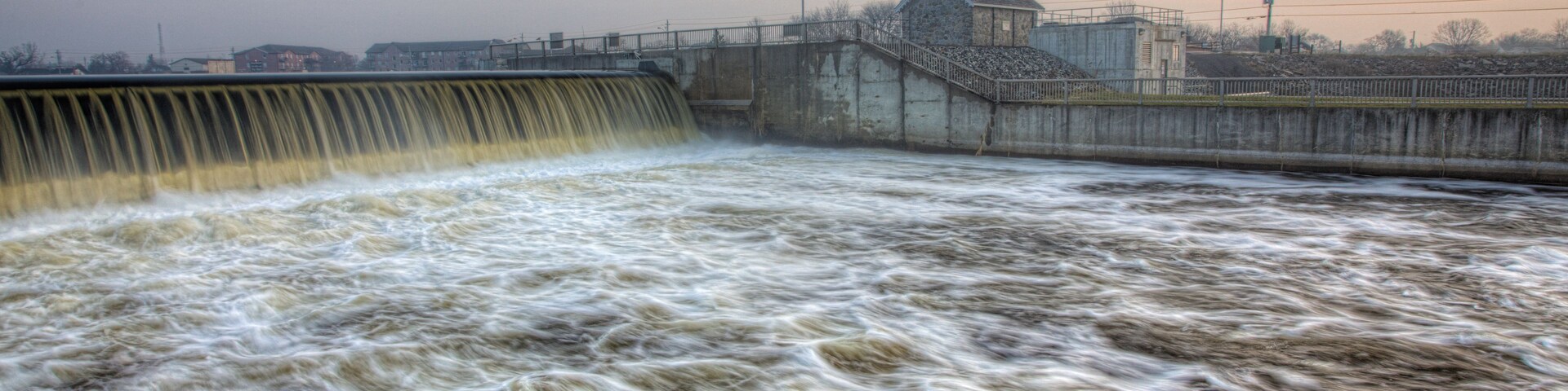 Una presa con una cascada, un puente y un edificio al fondo.