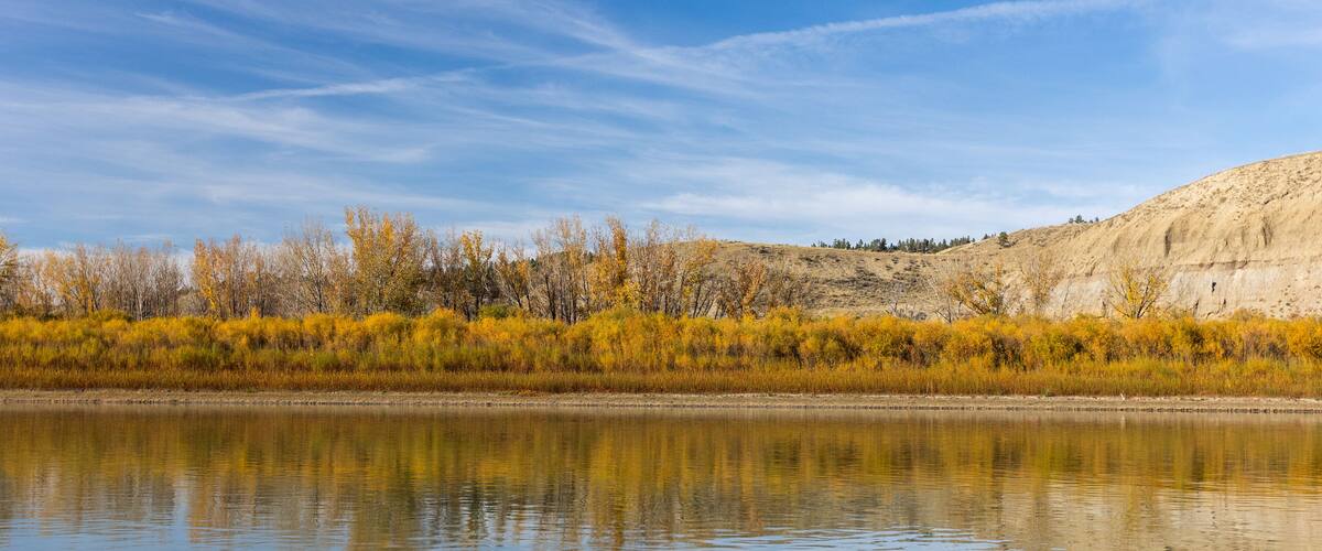 In Phillips County, Montana, autumn paints the riverbanks with vivid fall foliage, where colorful leaves reflect in calm waters under crisp skies.