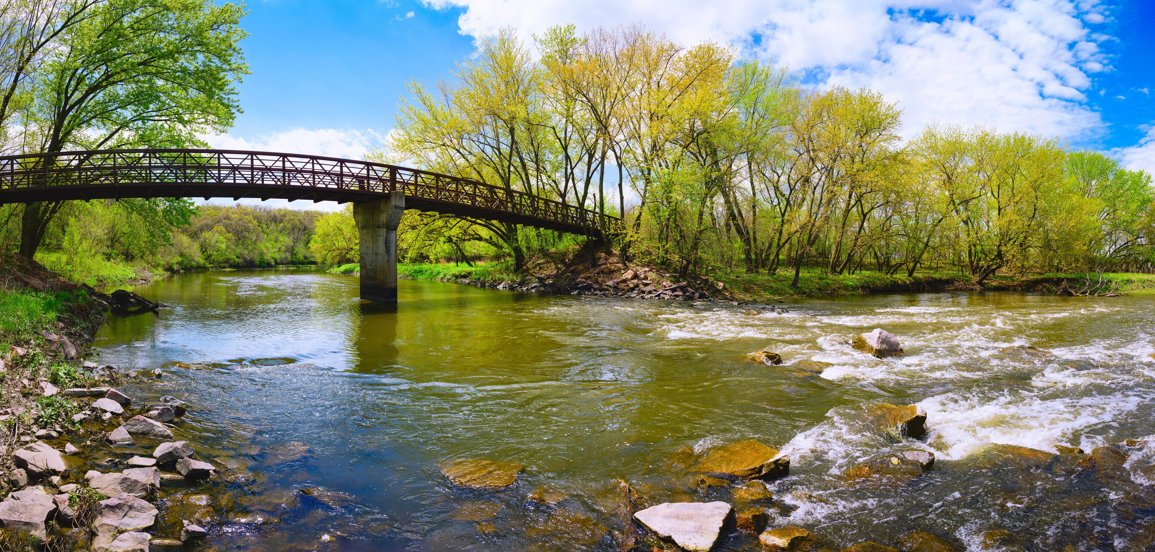 A wooden bridge over a river with rocks and trees.