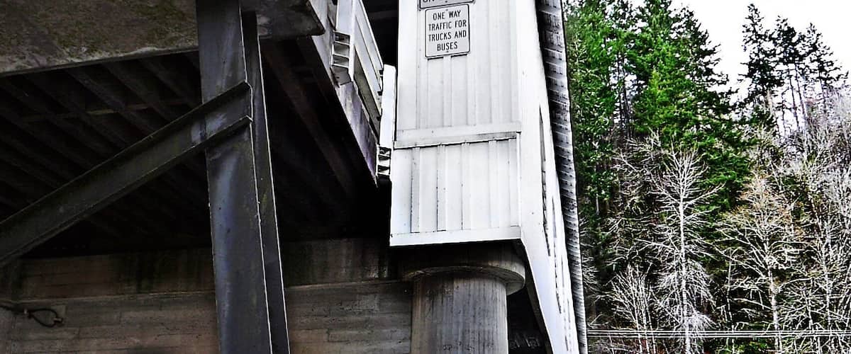 A bridge with a sign indicating one truck at a time on the bridge and one way traffic for trucks and buses.
