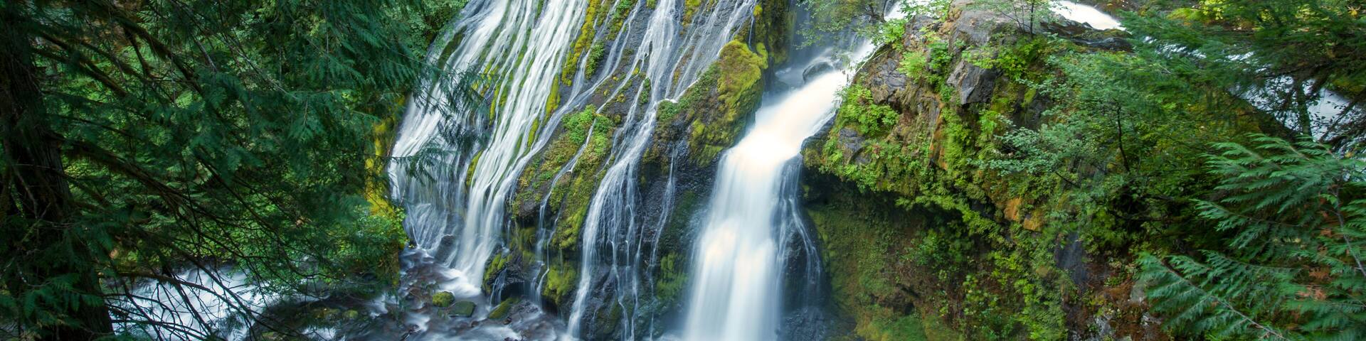 A multi-tiered waterfall surrounded by dense green forest.