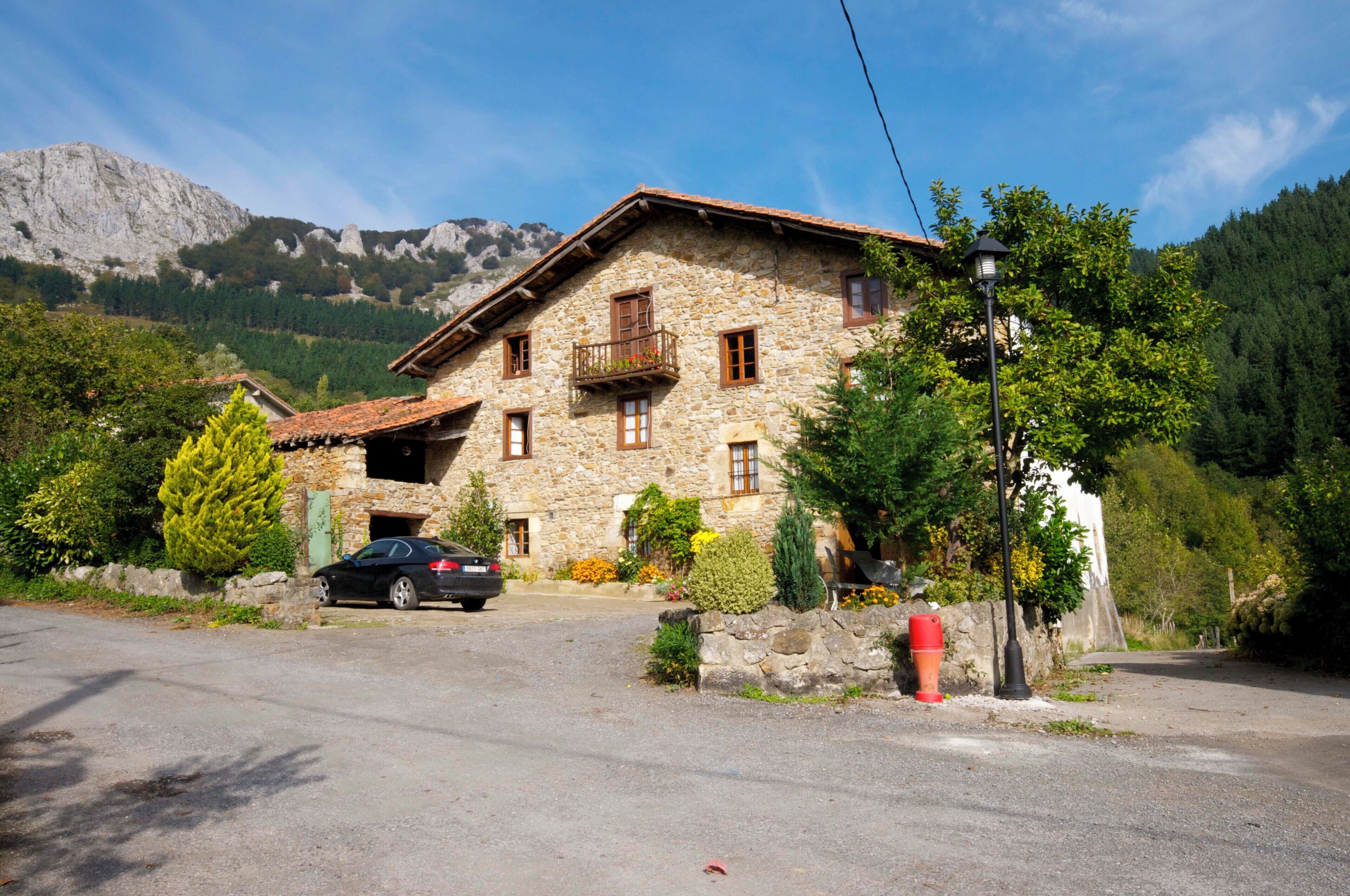 A stone house with a car parked in front, surrounded by trees and mountains.