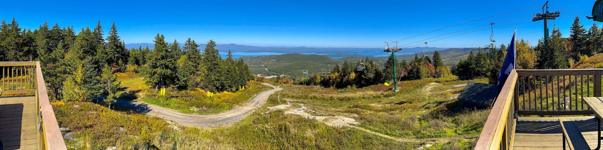 A mountain landscape with a ski lift, forested area, and a clear blue sky.