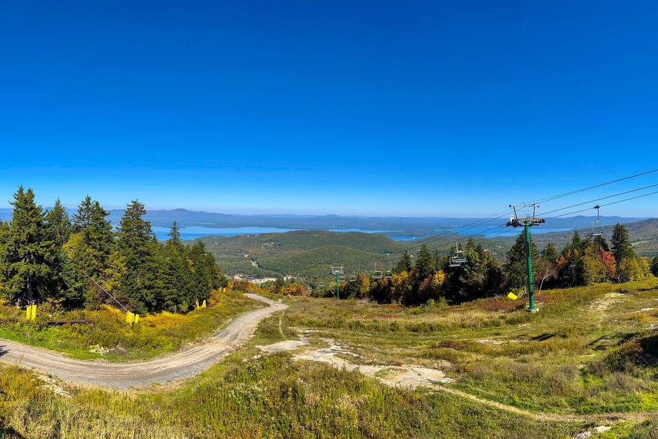 A mountain landscape with a ski lift, forested area, and a clear blue sky.