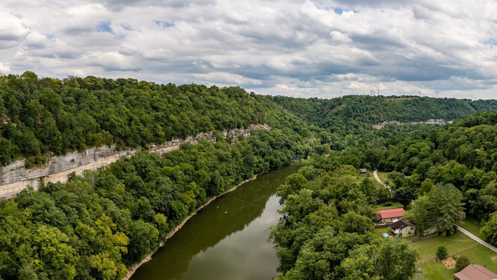 A river winding through a densely forested valley with a house and a red-roofed building near the water's edge.